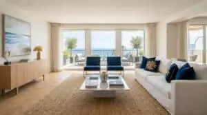 Salon lumineux et moderne avec grand canapé blanc, fauteuils bleus, table basse marbre et vue imprenable sur la mer.